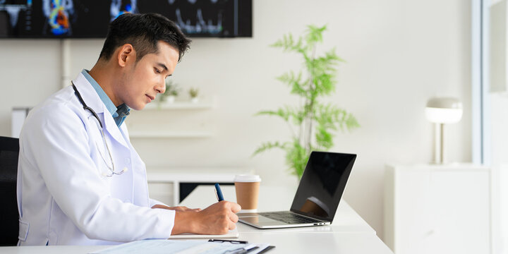 Doctor looking at laptop screen writing in notebook for research planning or medical tech innovation in hospital office. Healthcare medic worker, research strategy book notes and online communication.