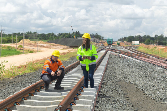 Asian engineers or workers wearing safety gear and hard hats, inspect railroad track construction at station, double-track railway construction in Thailand.