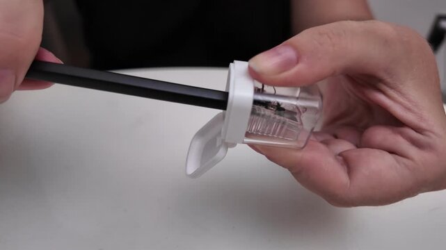 Close-up of a woman sharpening a pencil with a sharpener over a table.
