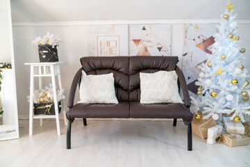 Christmas interior of a bright living room. The attic. A white Christmas tree with a brown sofa. Daytime.