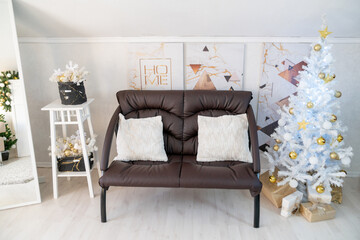 Christmas interior of a bright living room. The attic. A white Christmas tree with a brown sofa. Daytime.