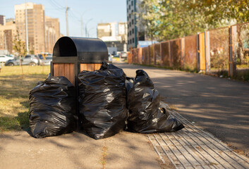 Obraz premium Trash can surrounded by a bunch of garbage bags on street. bags filled with trash on the street. dirty street concept, garbage collection, environmental pollution