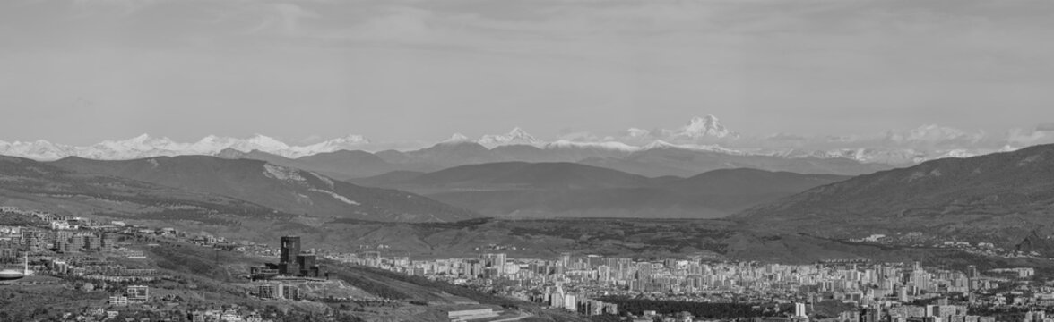 Fototapeta Black and white panorama of the cityscape of Tbilisi, capital of Georgia with snow-capped Caucasus mountains in the distance