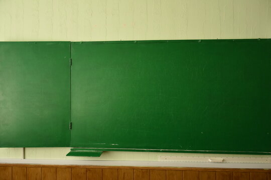 Close-up of a green school chalkboard on a light wooden wall. Educational background with copy space for text or design.