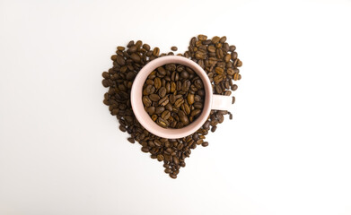 Heart shaped coffee beans with a pink mug isolated on white