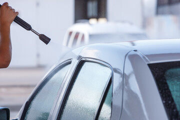 Washing car using a pressure washer on a sunny day in the city at self-service car wash station.
