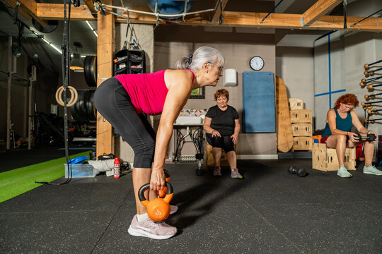 Senior woman lifting kettlebell during gym workout session - Powered by Adobe