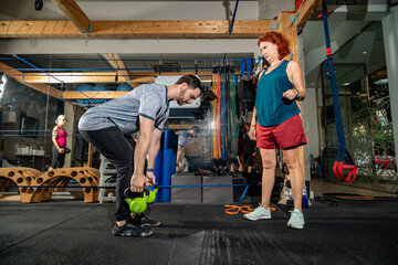 Man training with kettlebells under personal trainer guidance