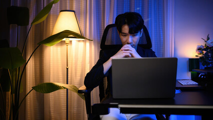 Professional man looking on a laptop after hours, illuminated by soft blue and warm light, concept of remote work and late night business tasks