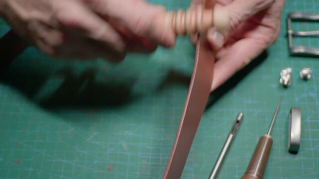A leather craftsman is making a belt, he is rubbing slicker on the edge of the leather