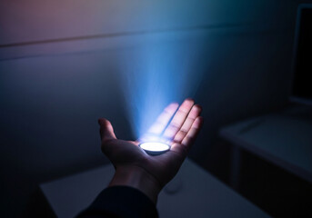 A hand holding a glowing object that emits a beam of light upwards.