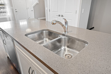 Stainless steel sink with a silver faucet sits on a granite countertop