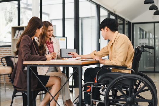 Young professional meeting with colleague wheelchair modern office table discussing project and showing tablet screen with friendly collaboration