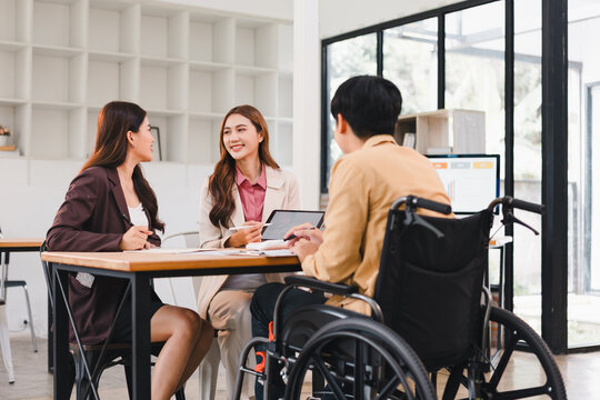 Young professional meeting businesswoman coworker tablet laptop wheelchair smiling collaborative discussion in modern office - Powered by Adobe