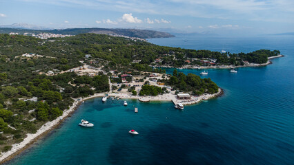 Obraz premium Aerial view of a beautiful coastal bay with yachts and sailboats anchored in clear turquoise water surrounded by green hills and seaside houses