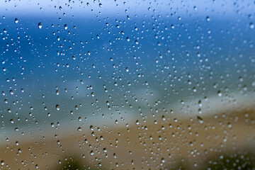 Gotas de lluvia cayendo sobre un cristal con el mar Mediterr&aacute;neo de fondo, creando una textura natural y atmosf&eacute;rica.