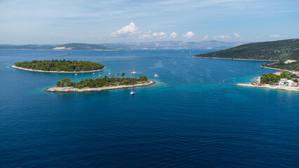 Obraz premium Aerial view of small green islands surrounded by deep blue sea with yachts and sailboats anchored near the rocky shore on a sunny day