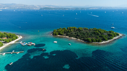 Aerial view of small green islands surrounded by deep blue sea with yachts and sailboats anchored near the rocky shore on a sunny day