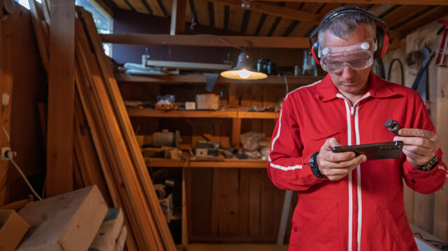 A man looks at a smartphone while holding a part in his hands.
