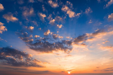 Stunning sunset sky with vibrant orange and blue hues, scattered clouds, and radiant sunbeams, capturing the awe-inspiring beauty and dramatic colors of the evening horizon.

