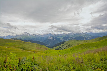 mountain landscape with green meadow and granite peaks with glaciers under a cloudy sky in La Vanoise nature reserve, Savoie, France 