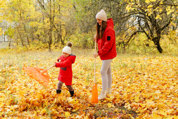 A child and an adult happily rake vibrant yellow and orange leaves in a park during autumn. The scene is cheerful and lively