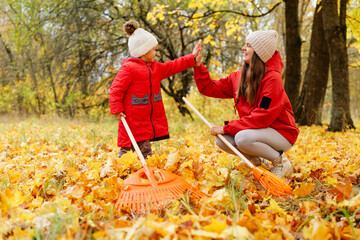 In a vibrant park, a mother and child share a joyful moment while raking yellow and orange leaves on a sunny autumn day