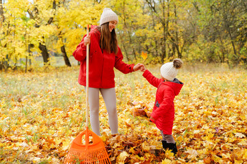A mother and child playfully interact while gathering colorful autumn leaves in a park filled with golden trees on a bright day