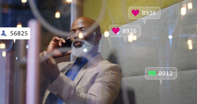 Talking businessman in suit holding smartphone in lounge, with pendant lights and social icons - Powered by Adobe