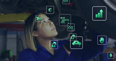 Inspecting mechanic in blue coverall and gloves under vehicle in garage with floating data icons