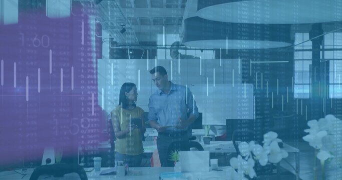 Two business professionals reviewing data overlay in open-plan workspace, with laptops