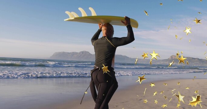 Walking surfer in black wetsuit carrying yellow surfboard with fins on beach, with star confetti