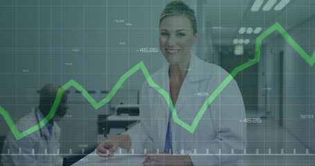 Smiling doctor wearing lab coat writing on clipboard in clinic corridor with green graph overlay