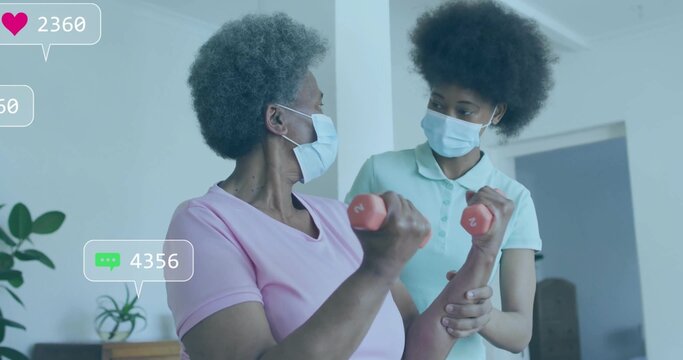 Guiding therapist supporting masked senior woman lifting red dumbbells at home, with overlay icons