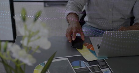 Designer in shirt with rolled sleeves selecting color from swatch at office desk, laptop layouts