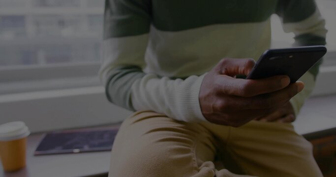 Looking at smartphone man in sweater on window ledge, with coffee cup and magazine, copy space