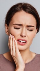 Fototapeta premium Young woman feeling intense pain, holding her cheek while eyes are closed and face is contorted, symbolizing toothache, dental problems, and discomfort
