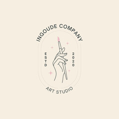 Elegant hand holding paintbrush in minimalist art studio logo for creative brands