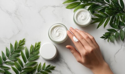 Hand applying cream near two jars on a marble surface with leaves