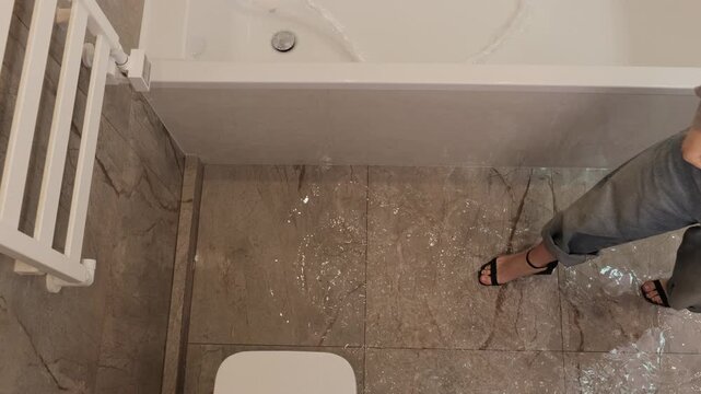 Bathroom flooding, plumbing failure, wet floor. Water leaking from bathtub flooding bathroom floor, with person stepping in water. Concept plumbing issue or home emergency.