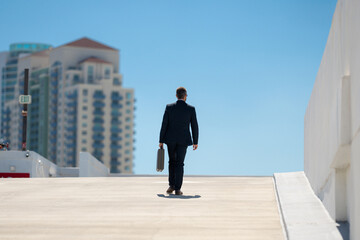 Back view of business man with briefcase walking. Business man walking away. Corporate leader go away. Man in suit with briefcase. Business professional from behind. Urban business man.