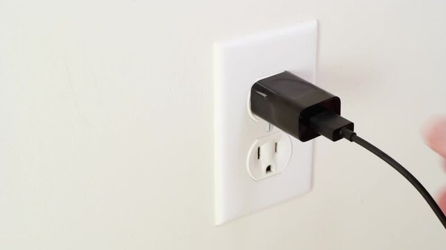 Close-up of hand inserting USB adapter plug into wall outlet. Tight framing highlights grip and connection.