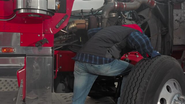 Mechanic Repairs Engine of Red Truck in Busy Garage