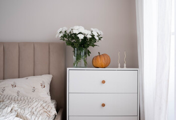 A serene bedroom with a charming nightstand and delicate white Chrysanthemum flowers, decorative pumpkin perfect for relaxation and comfort.