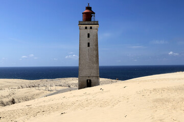 Landscape photo with a view of the Rubjerg Knude lighthouse (also known as the "Lighthouse in the Dunes") with sand dunes in the foreground against a blue sky with clouds near Lokken in Denmark