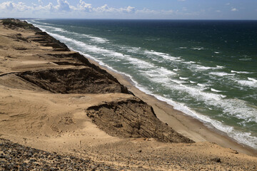 Landscape photo with a view of the North Sea coast and sand dunes against a blue sky with clouds near the Rubjerg Knude lighthouse in Denmark