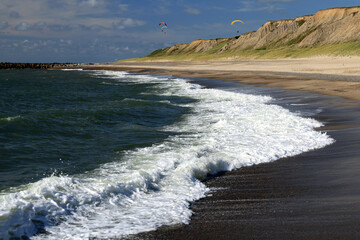Landscape photo with a view of the North Sea coast, beach and paragliders in the background against a blue sky with clouds near Bovbjerg Lighthouse in Lemvig, Denmark