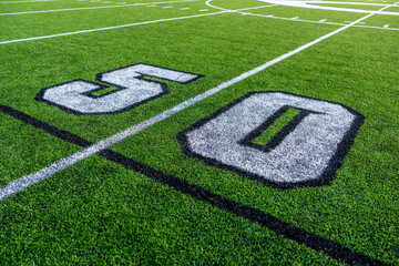 Green synthetic turf football 50 yard line, block number, in white along with black lacrosse line.	