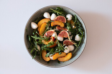 A beautifully vibrant salad composed of fresh peaches, creamy mozzarella, sweet figs, and peppery arugula on white background.