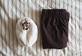 A wonderfully cozy loungewear set that includes warm pants and fluffy woman cosmetique bag sitting on a soft, inviting bed.